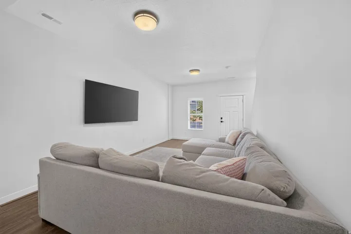 Bright, open room featuring a mounted flat-screen panel, wood-finish flooring, and white walls