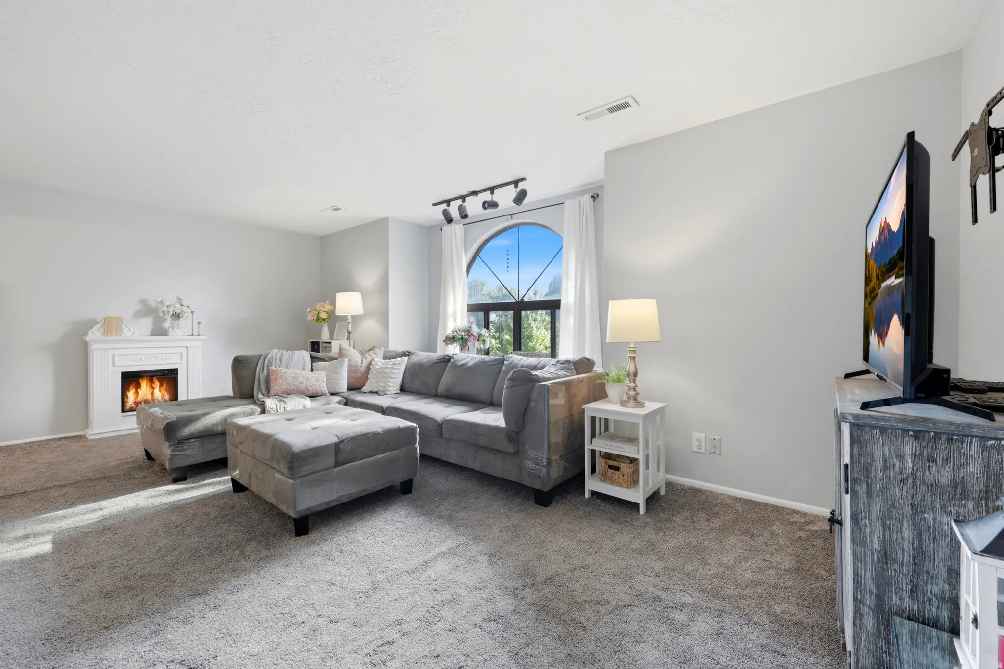 Carpeted living space featuring an arched window, white trim, and a decorative fireplace