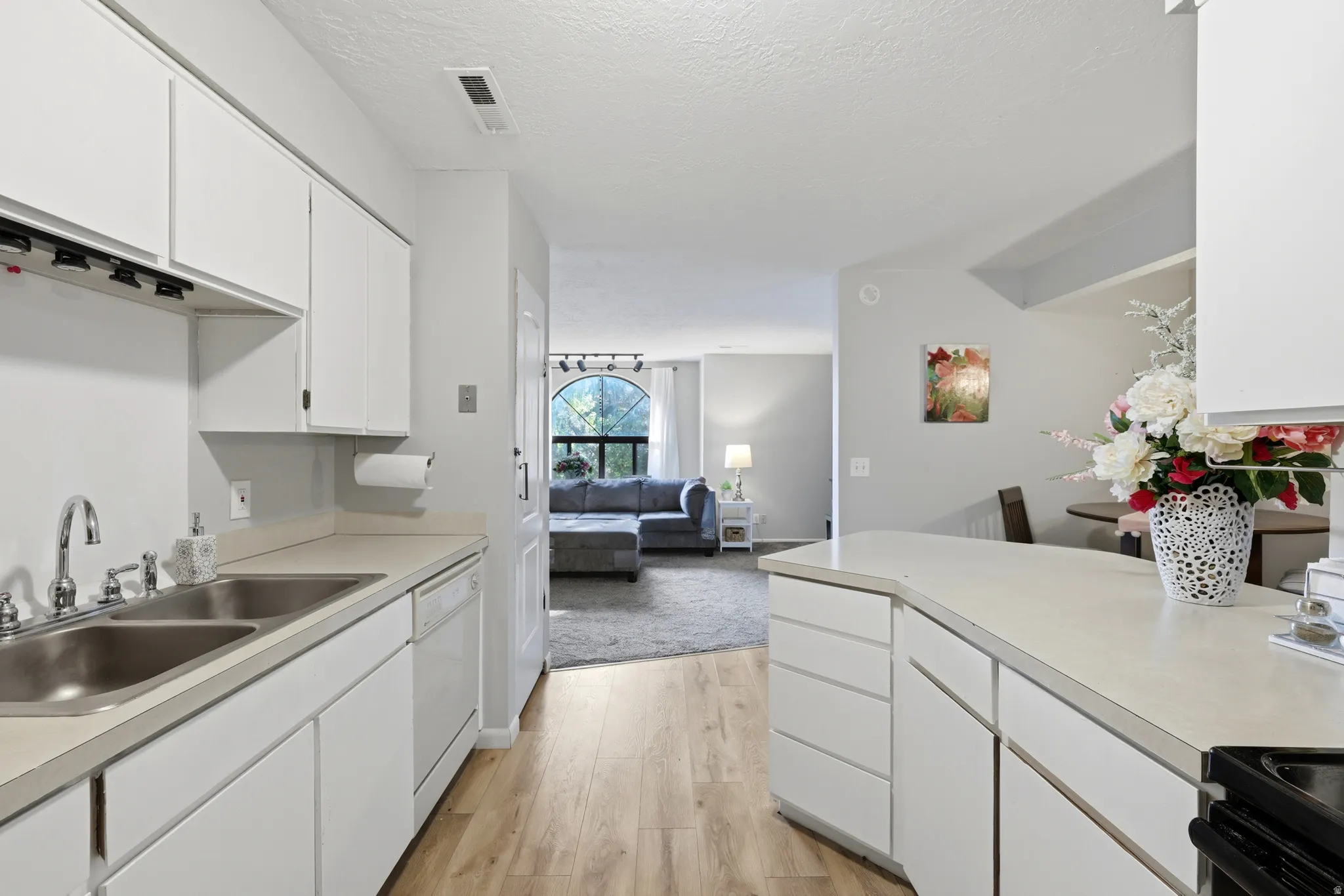 Kitchen featuring white cabinetry, light-toned countertops, a double basin stainless steel sink, and wood-finish flooring