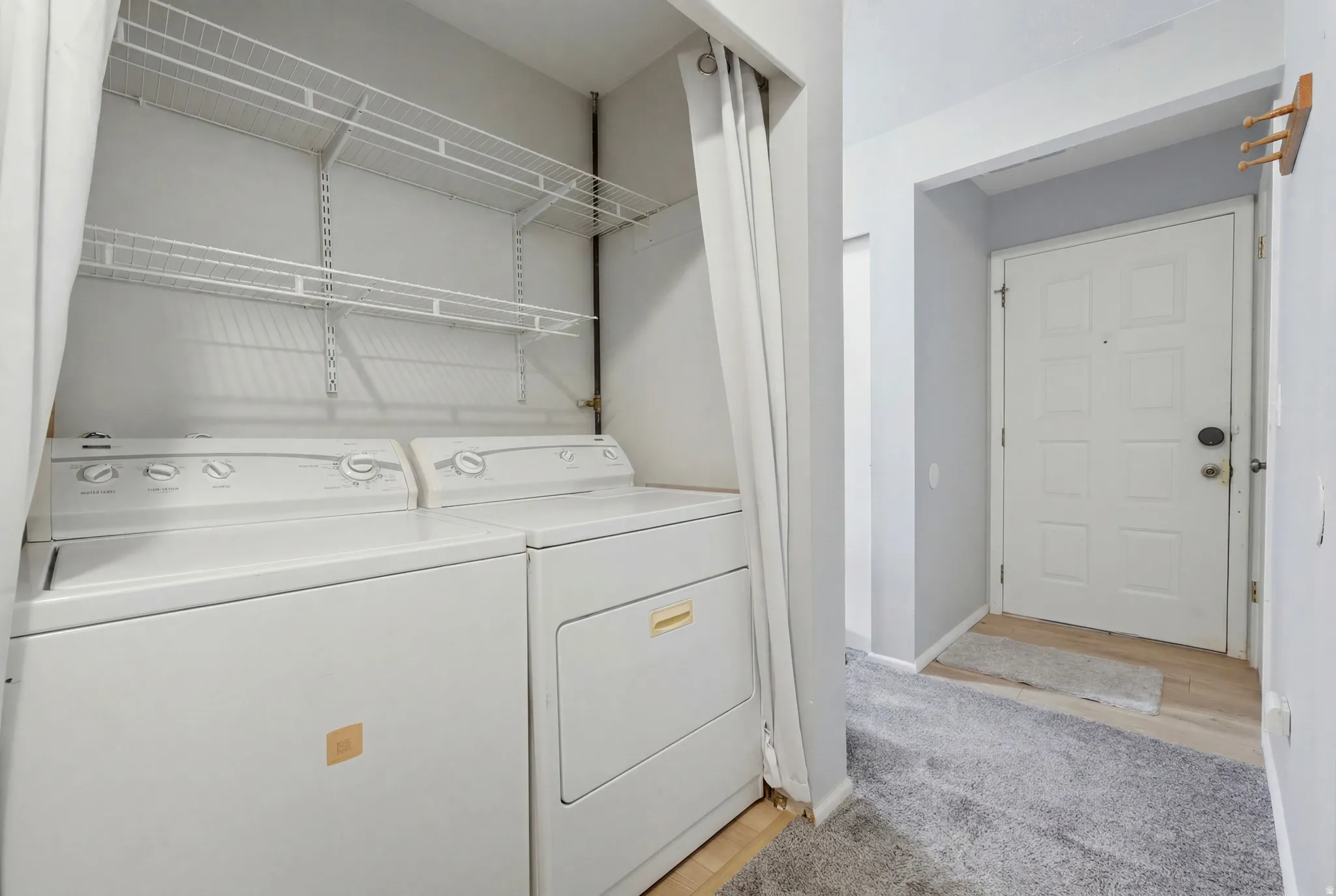 Dedicated laundry area featuring a washer and dryer, integrated shelving, and a privacy curtain