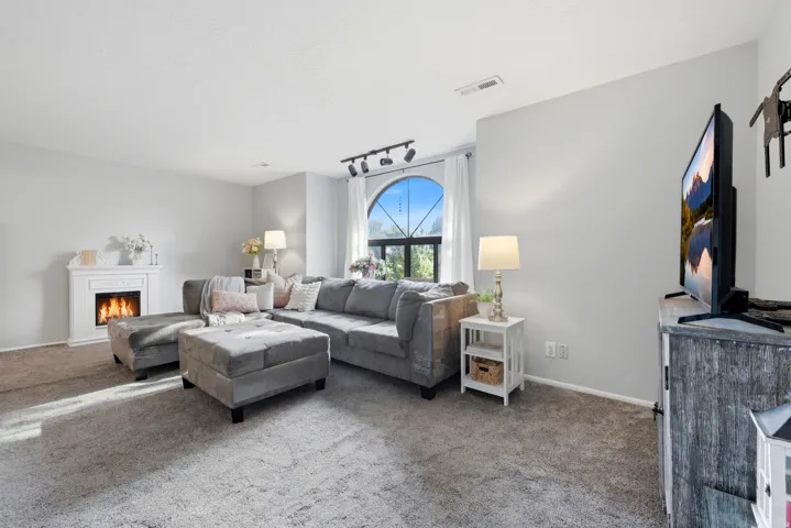Carpeted living space featuring an arched window, white trim, and a decorative fireplace
