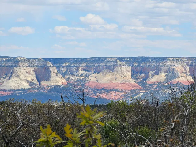 Expansive natural landscape with layered rock formations featuring white, red, and beige strata