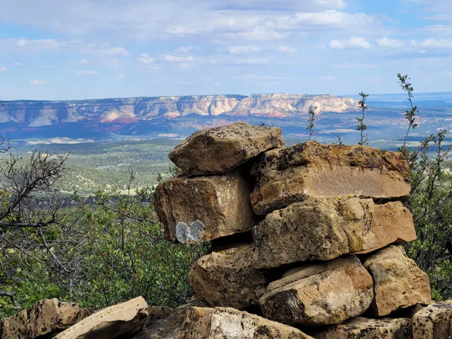 Stacked natural rock formation in the foreground, with a distant layered mesa under a partly cloudy sky