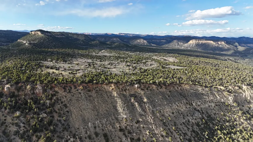 Expansive natural landscape featuring rolling hills and distant mesas under a blue sky with scattered clouds