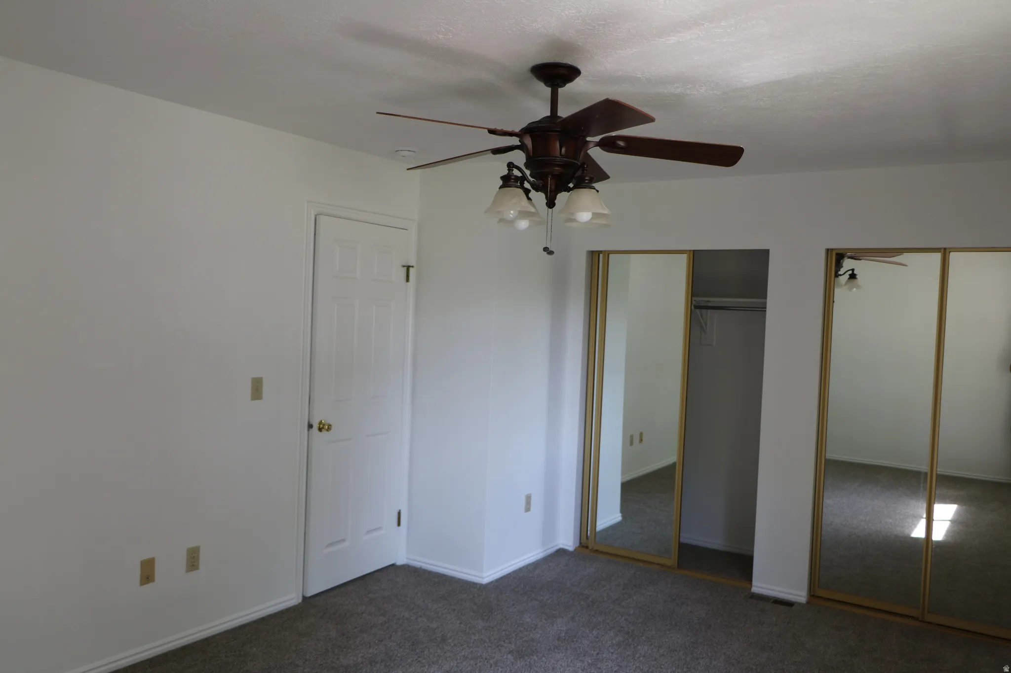Room featuring a ceiling fan with integrated lighting, textured white walls, and a multi-panel door with brass hardware