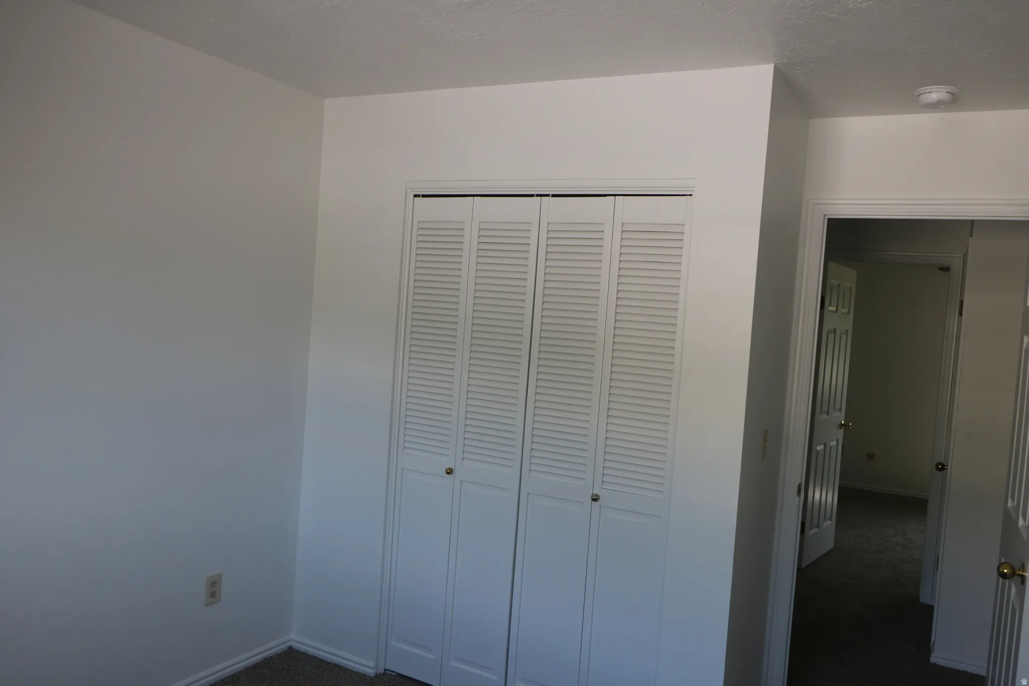 Louvered bi-fold closet doors, neutral wall paint, white trim, and carpeted flooring