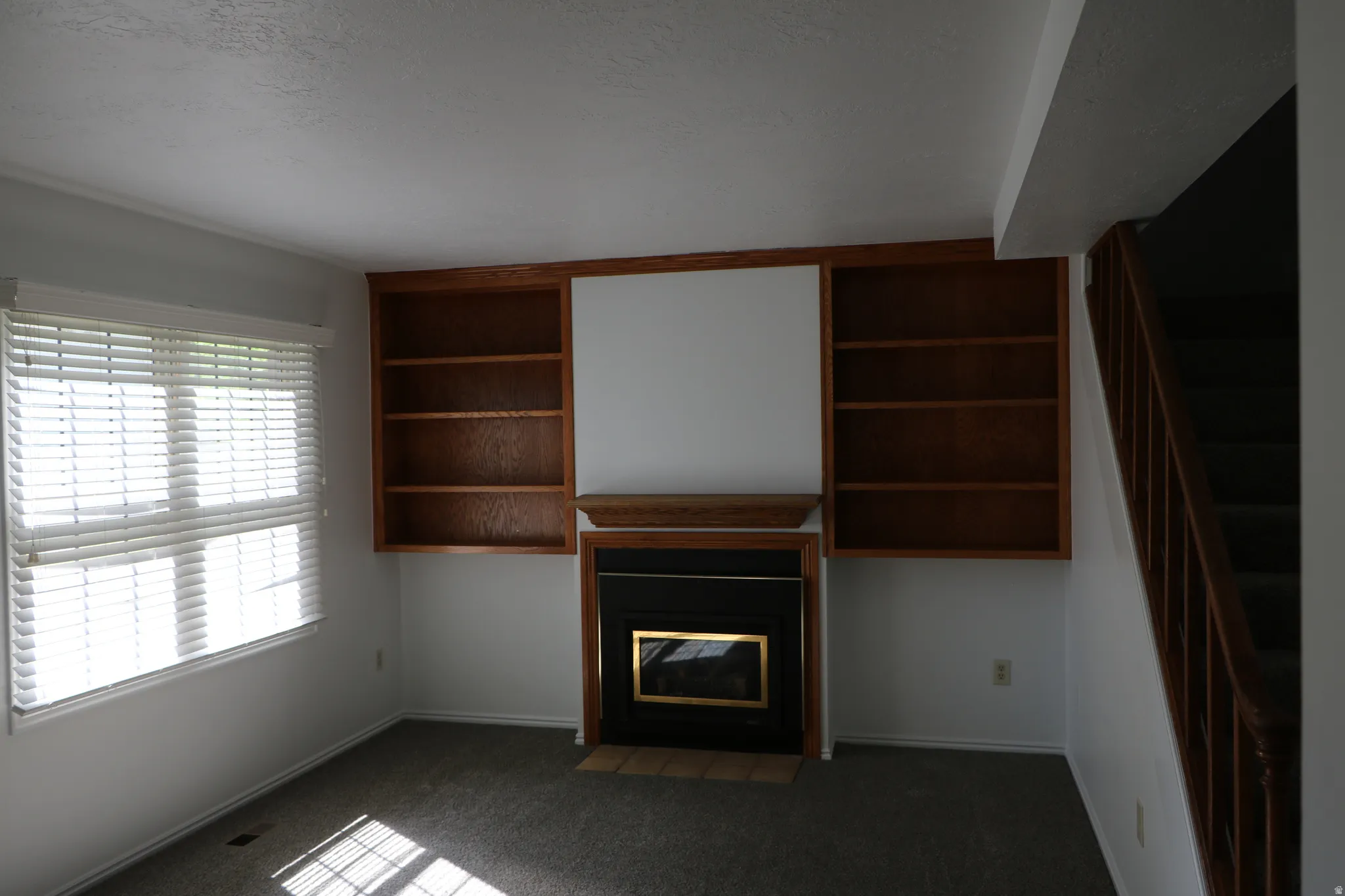 Living area featuring a fireplace with a brass-trimmed insert, flanked by built-in wooden shelving units, and a window with white blinds