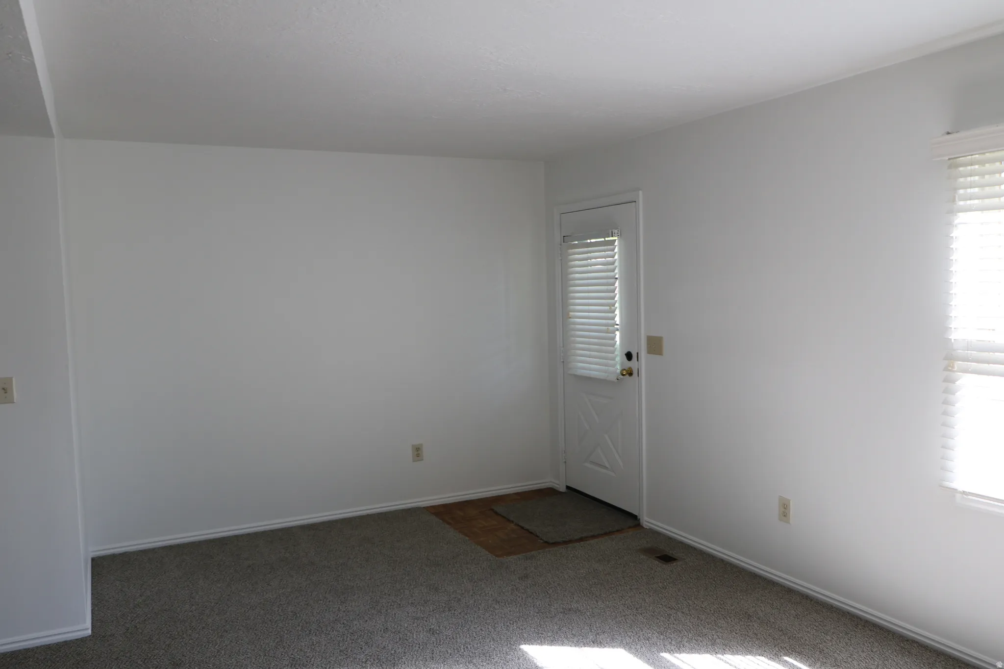 Living area featuring plush carpeting and white painted walls, a white paneled door with integrated blinds, and a window with horizontal blinds