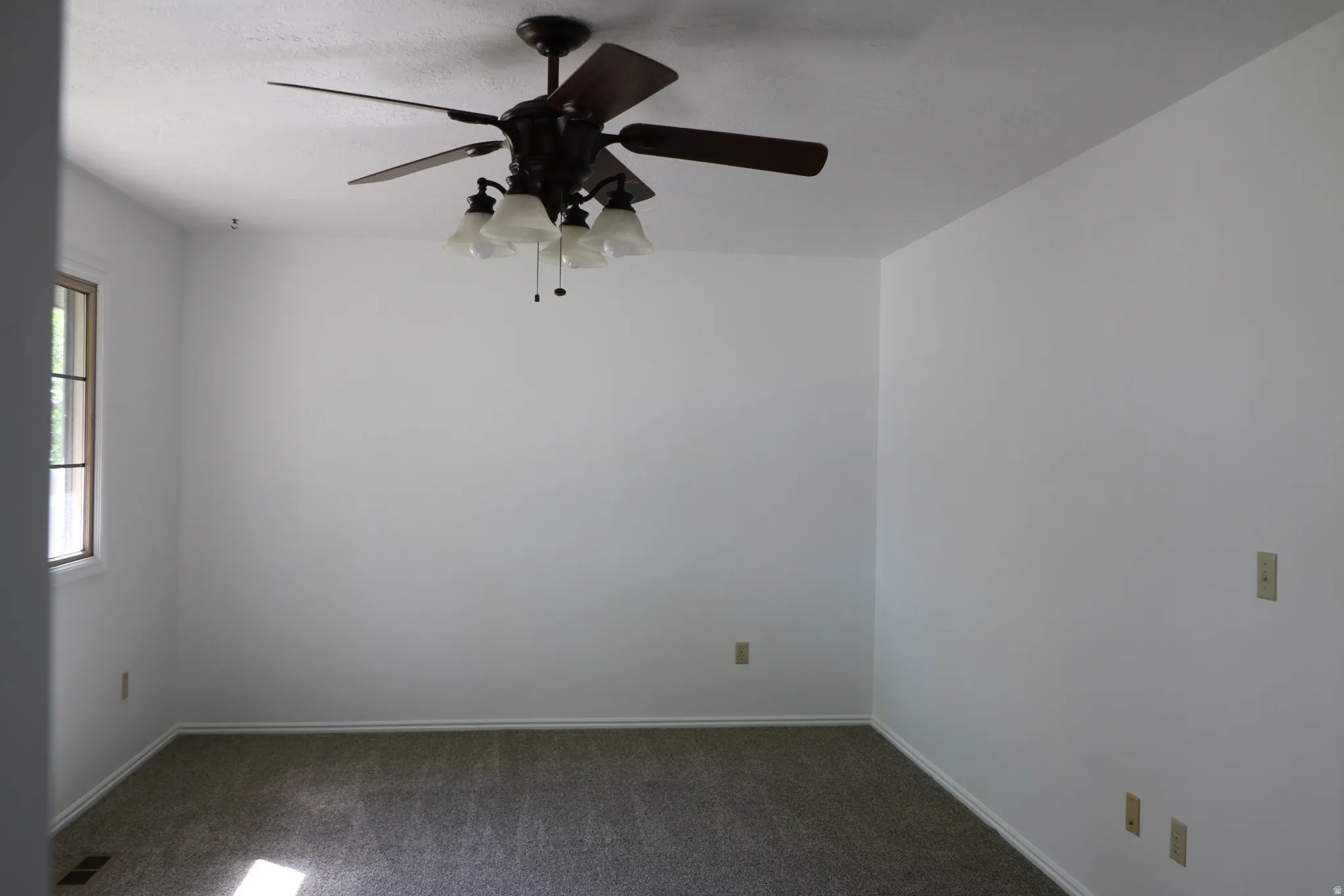 Spacious interior room featuring white walls, textured carpeting, and a ceiling fan with integrated lighting