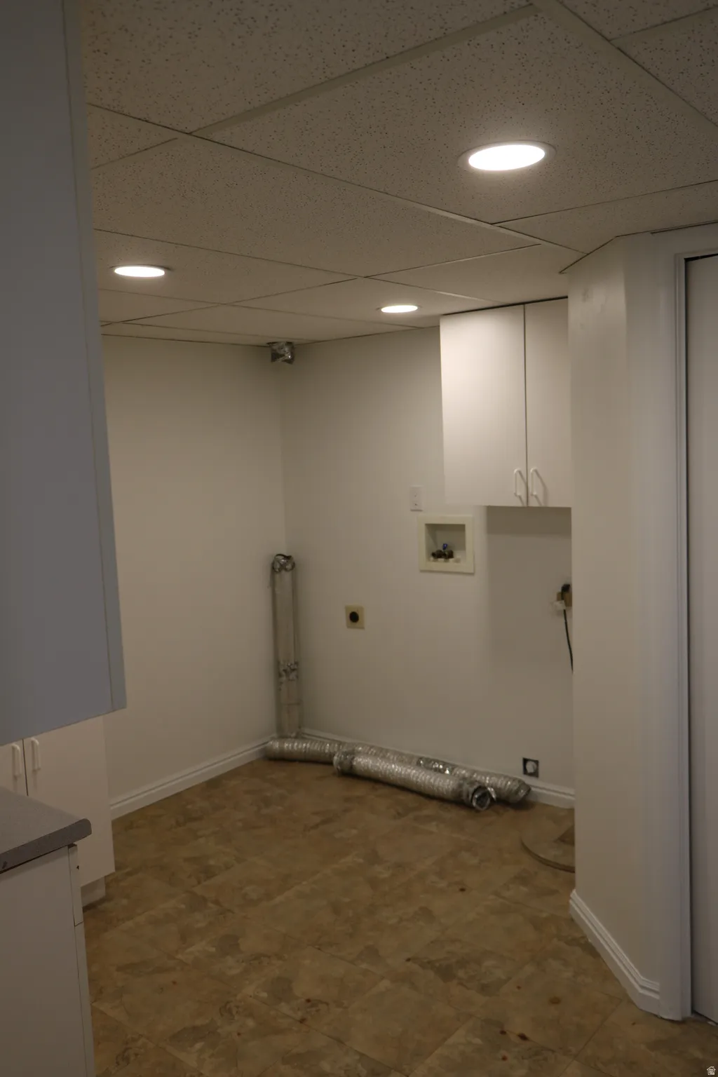 Dedicated laundry room featuring a drop ceiling with recessed lighting, white cabinetry, a utility sink, and durable vinyl flooring