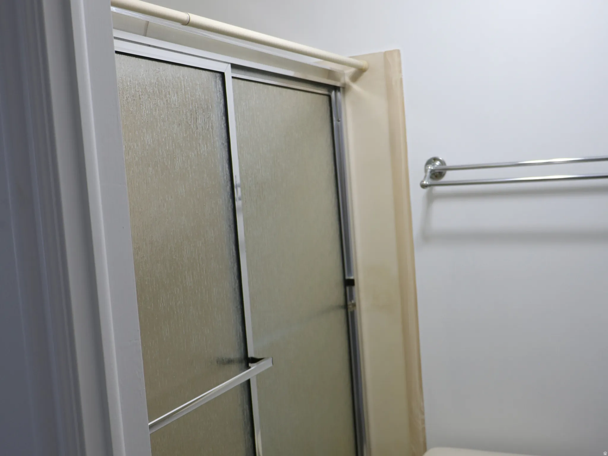 Bathroom featuring a white toilet, chrome towel bar, and a shower enclosure with frosted glass sliding doors