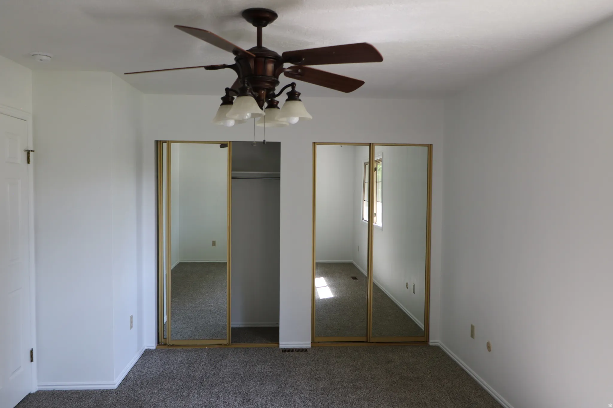 Bedroom featuring a ceiling fan with integrated lighting, carpet flooring, a white paneled door, and two mirrored sliding closet doors with gold-finish frames