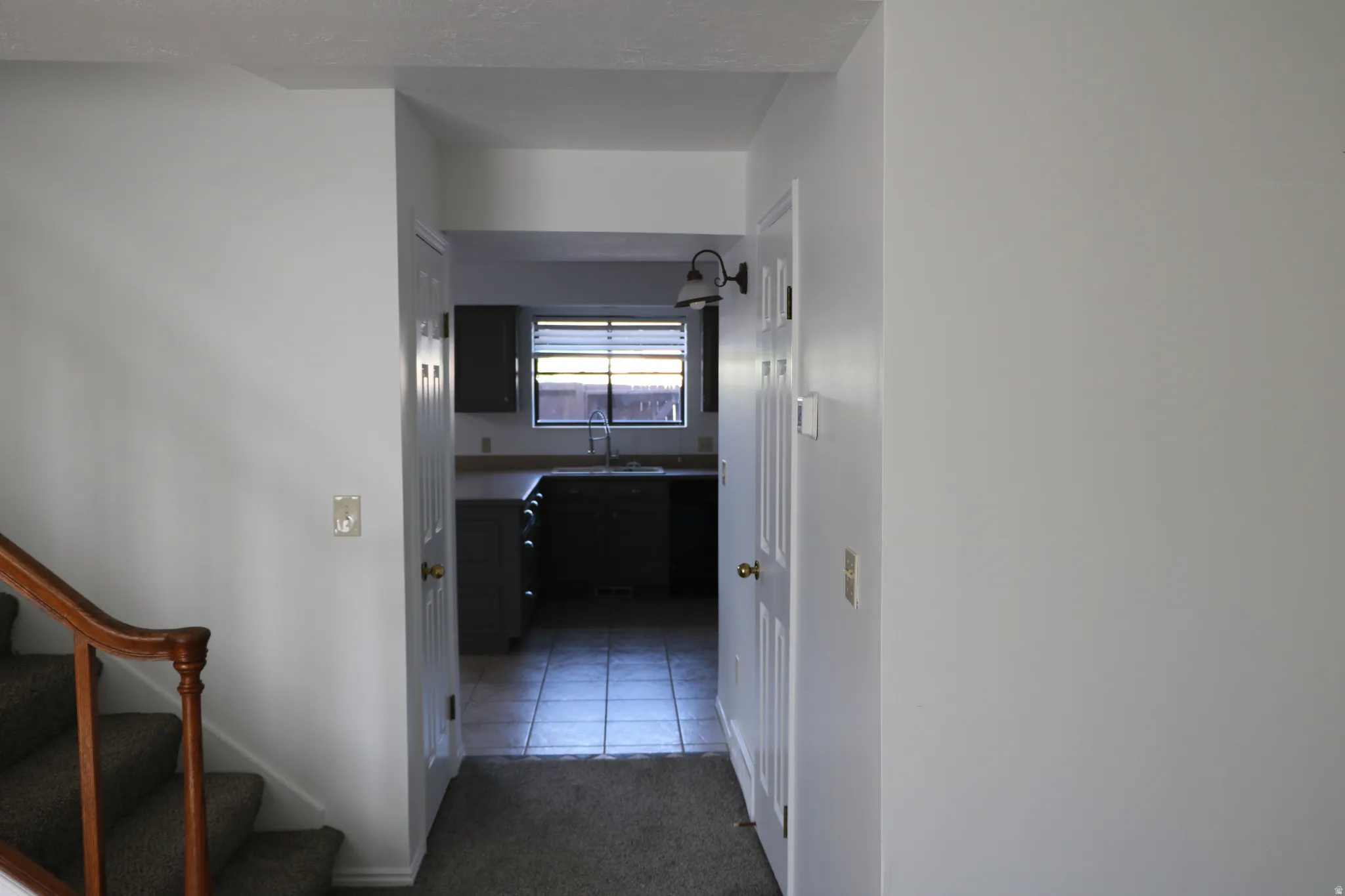 Kitchen entry featuring a dark wood-finish cabinet, window with horizontal blinds, stainless steel sink, and wall-mounted light fixture