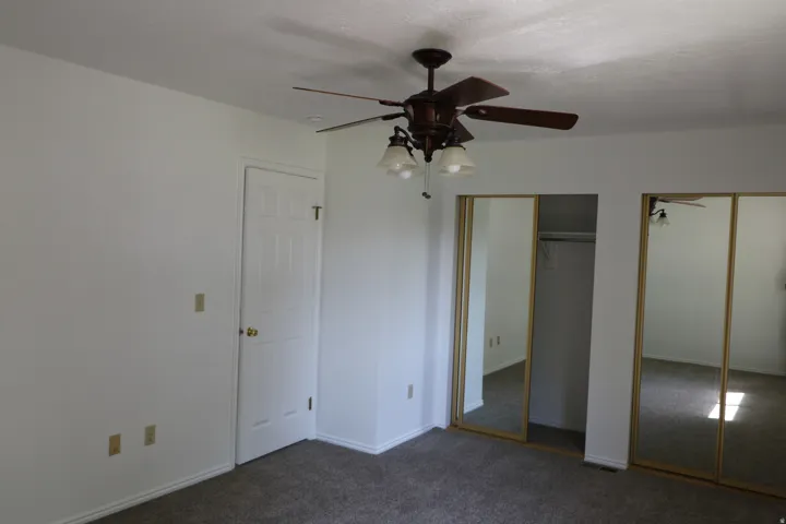 Room featuring a ceiling fan with integrated lighting, textured white walls, and a multi-panel door with brass hardware