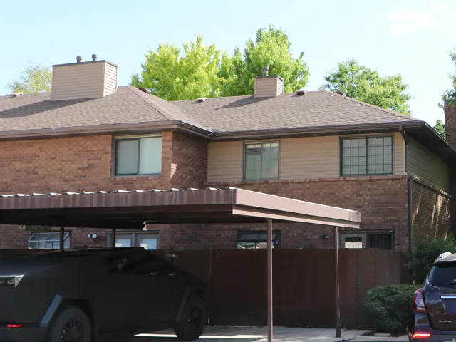 Brick exterior residence featuring a covered carport, pitched shingle roof, and multiple windows