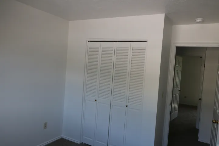 Louvered bi-fold closet doors, neutral wall paint, white trim, and carpeted flooring