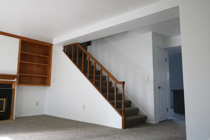 Carpeted staircase with wood railing, built-in shelving, and a dark-toned fireplace surround