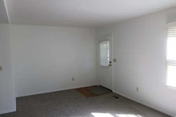 Living area featuring plush carpeting and white painted walls, a white paneled door with integrated blinds, and a window with horizontal blinds