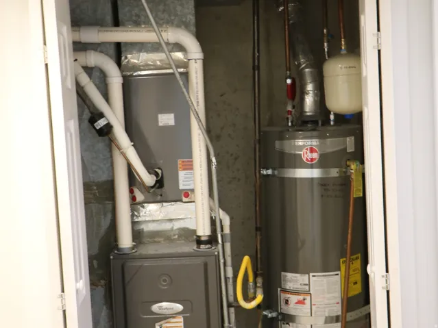 Utility closet housing a water heater and HVAC unit, featuring white louvered bifold doors and textured tile flooring