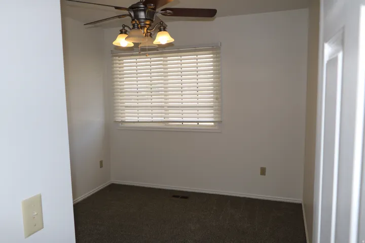 Neutral carpeted room featuring a ceiling fan with integrated lighting, a window with horizontal blinds, and white baseboards