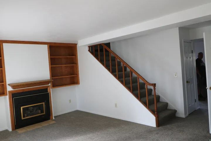 Living area featuring a staircase with wood railing, built-in shelving, a fireplace with a black surround and brass accent, and grey carpeting