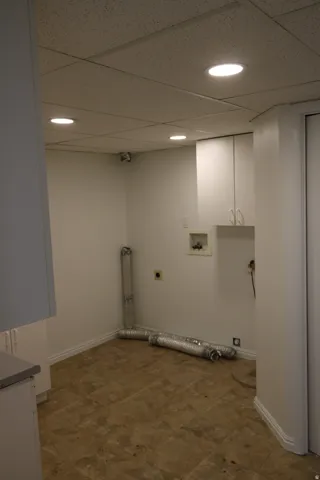 Dedicated laundry room featuring a drop ceiling with recessed lighting, white cabinetry, a utility sink, and durable vinyl flooring