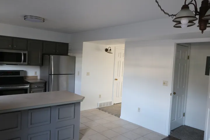 Kitchen featuring stainless steel appliances, grey cabinetry, a functional island with a light-toned countertop, and light-toned tile flooring