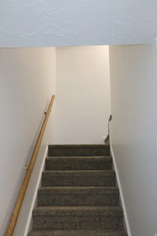 Carpeted staircase with a wood-finish handrail, neutral wall paint, and a textured ceiling finish