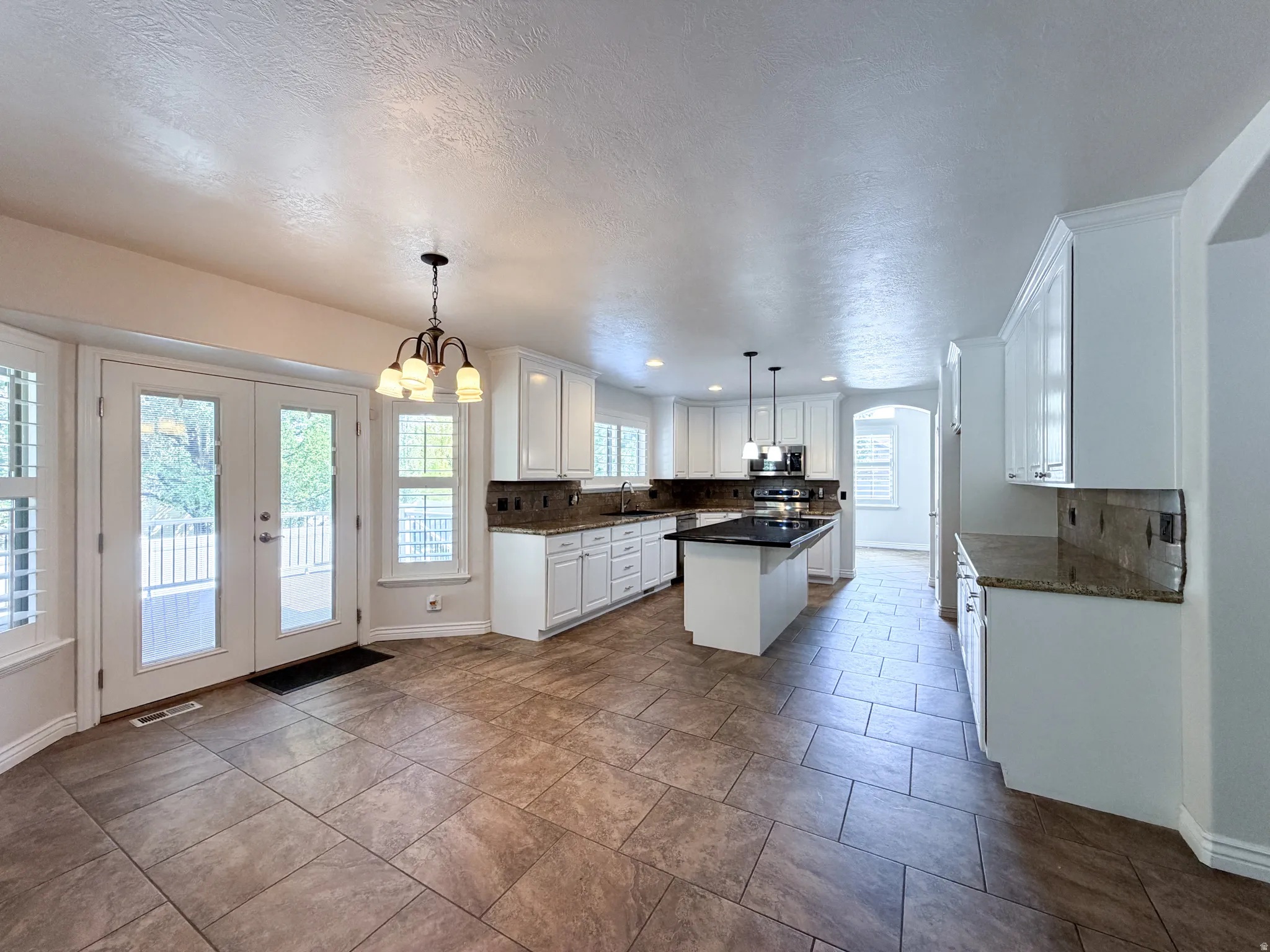 Spacious kitchen featuring white cabinetry, granite countertops, tile flooring, a central island with a dark countertop, and French doors opening to an outdoor deck