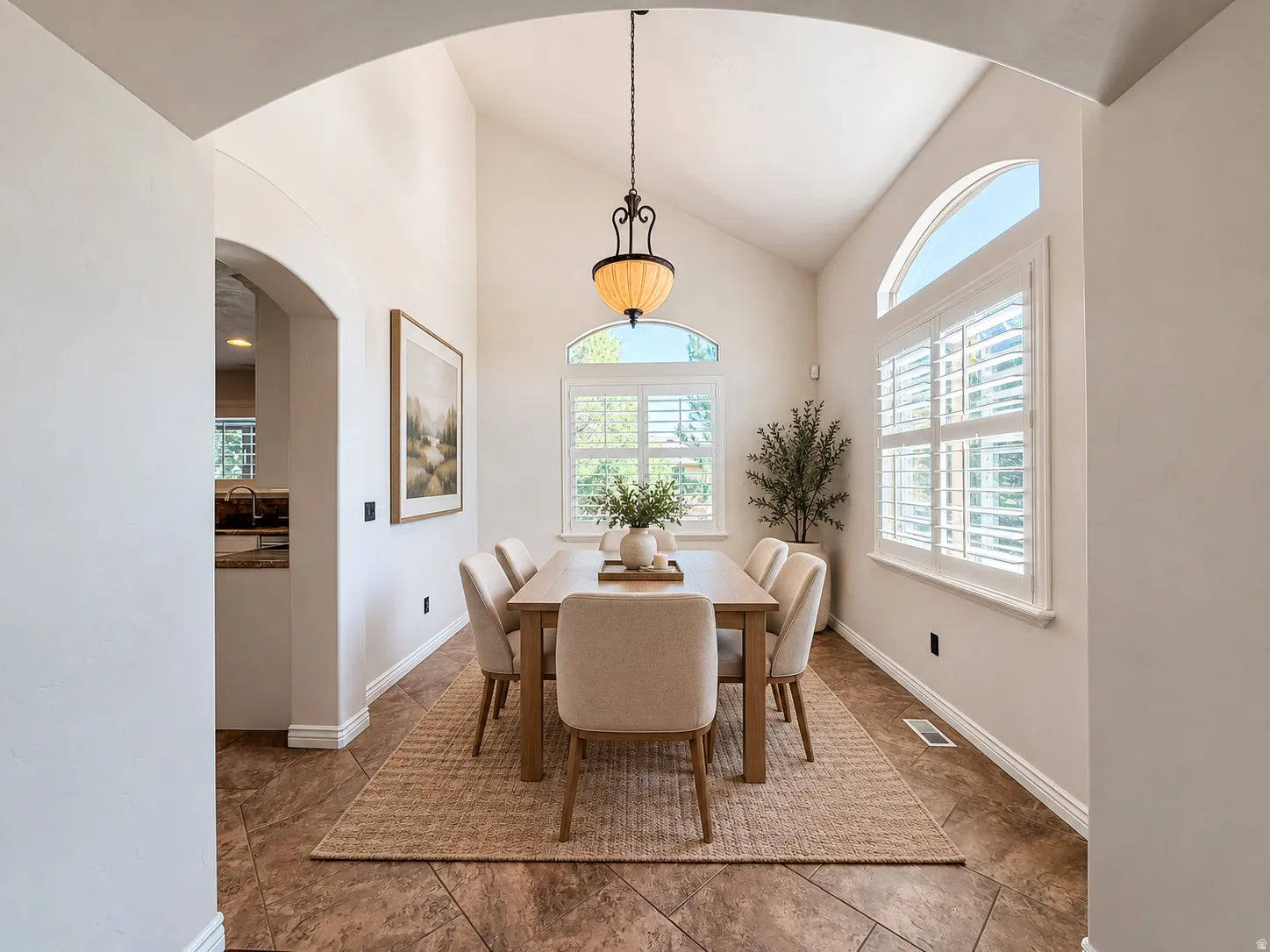 Dining area featuring vaulted ceilings, arched windows with plantation shutters, a decorative pendant light fixture, and tile flooring