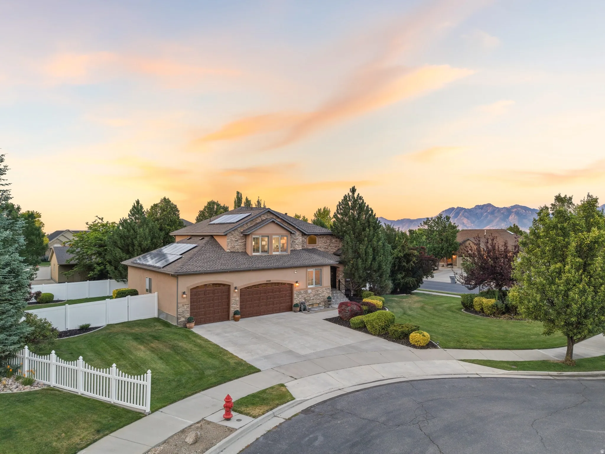Two-story residence featuring a stucco and stone facade, a two-car garage with arched wood-finish doors, and solar panels