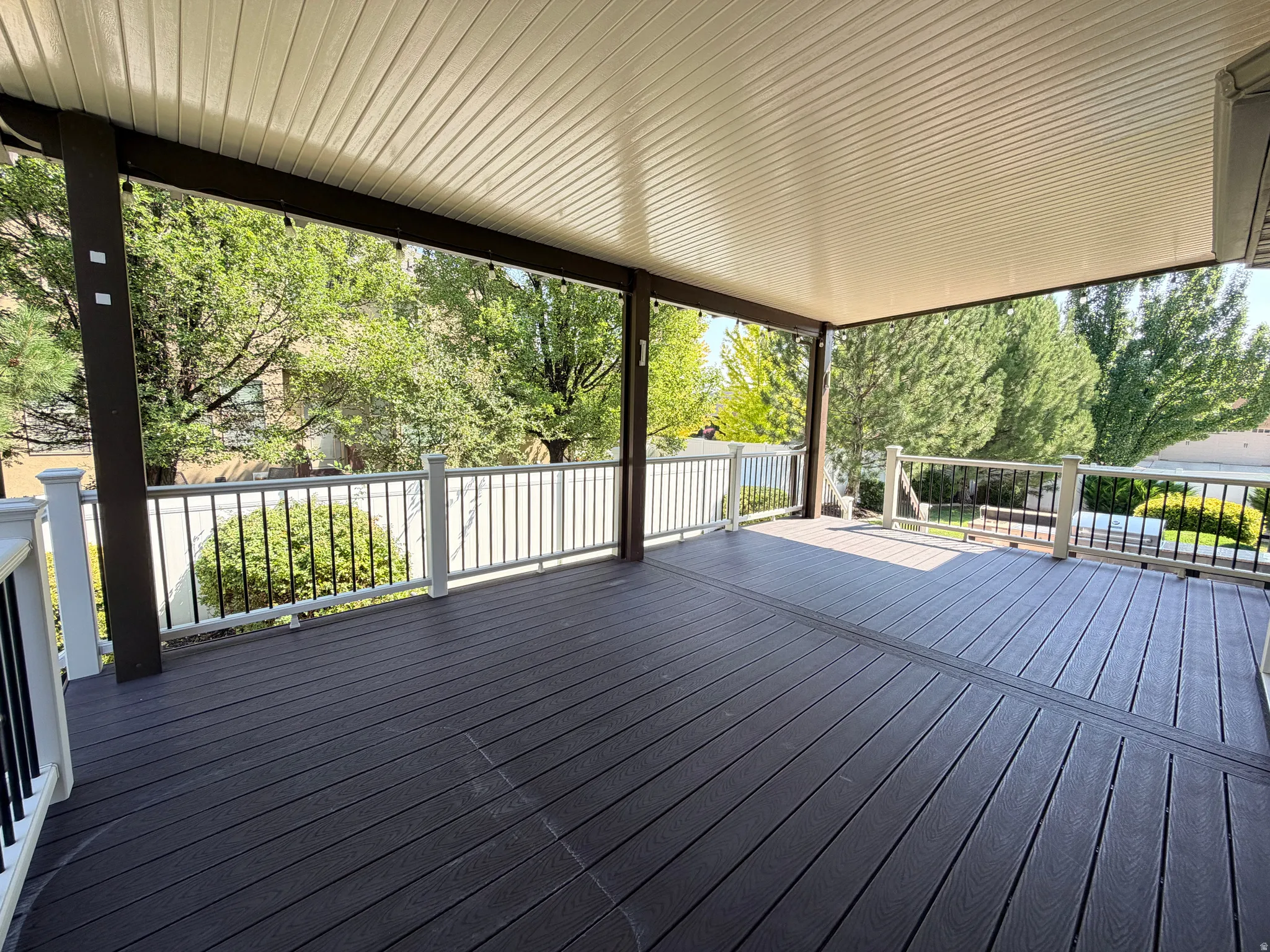 Expansive composite deck featuring dark wood-finish decking with linear board pattern, topped by a modern metal-framed pergola with integrated shade panels