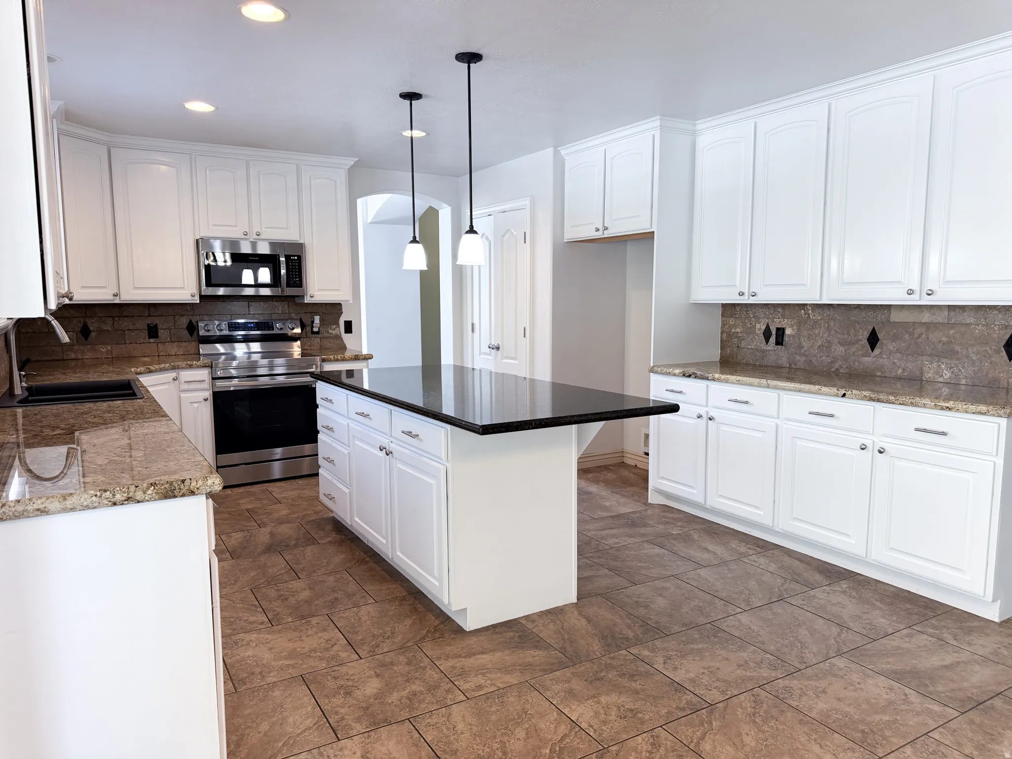 Kitchen featuring white cabinetry, granite countertops, tile flooring, stainless steel appliances, and a central island with a dark countertop