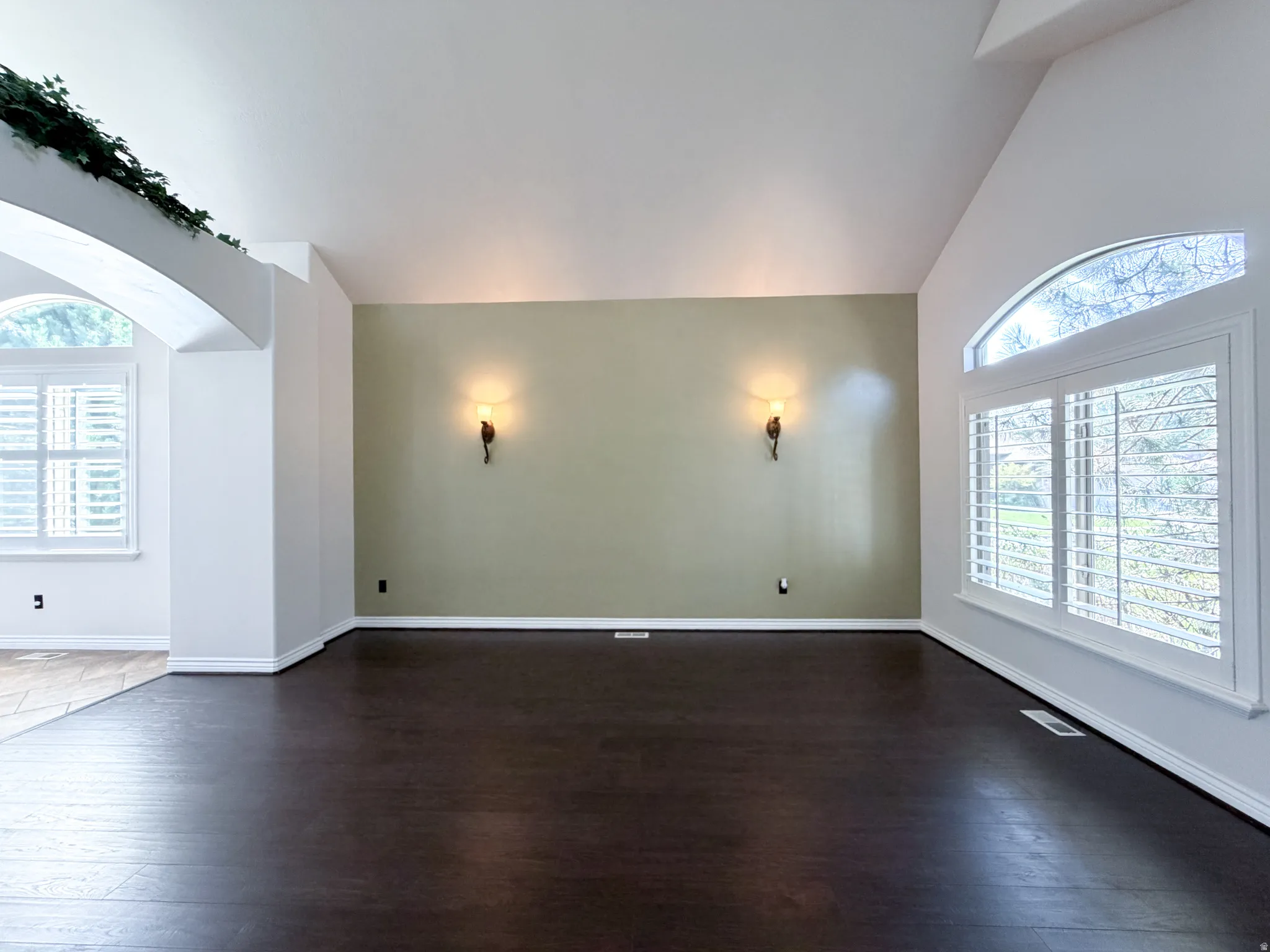 Vaulted ceilings, wood-finish flooring, arched windows with plantation shutters, and decorative wall sconces