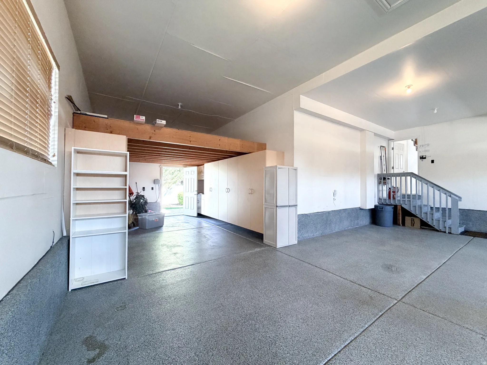 Epoxy-coated concrete flooring, built-in cabinetry, overhead storage loft, staircase access, and a large window with blinds