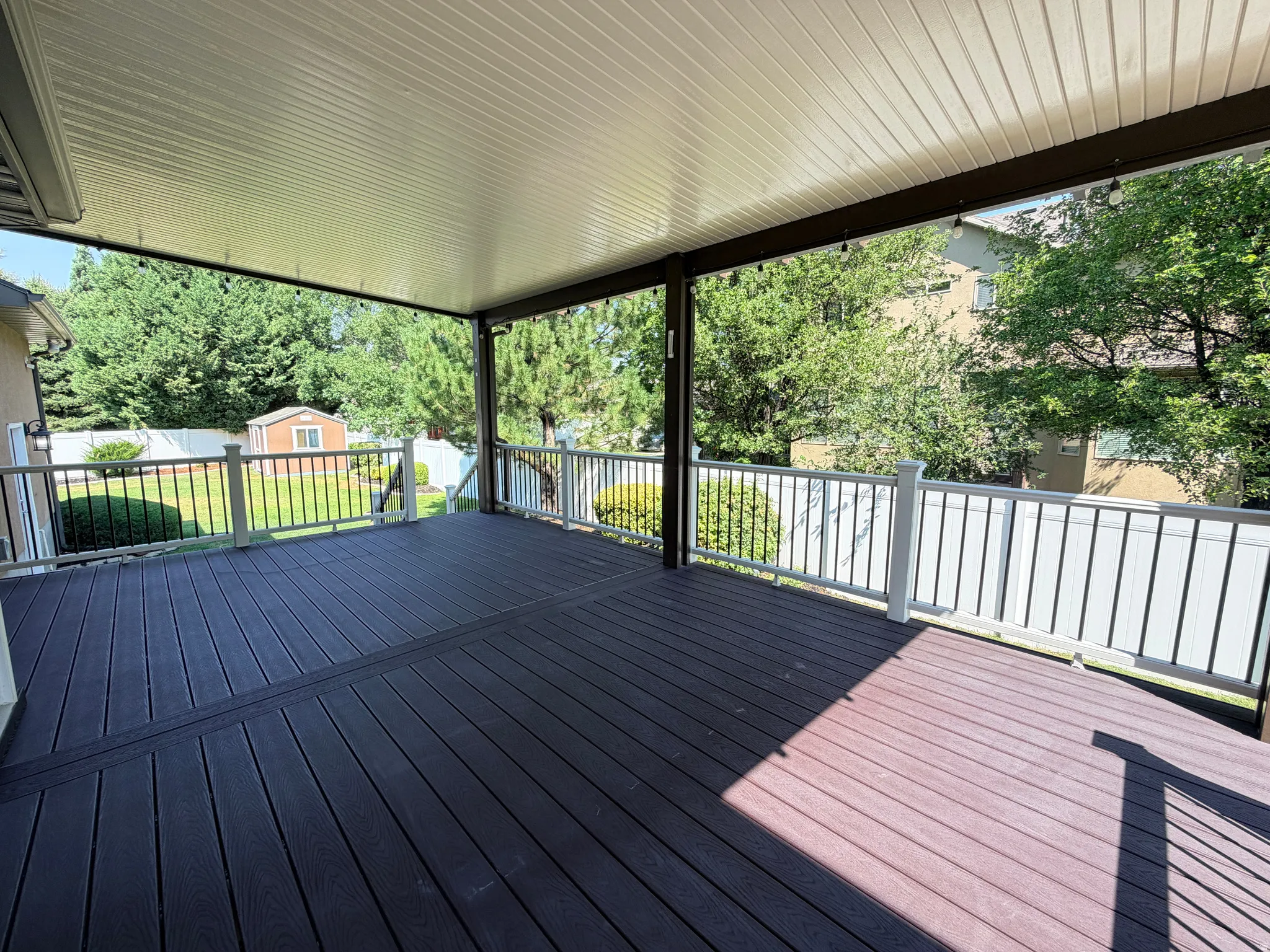 Expansive covered deck featuring composite decking in contrasting finishes, aluminum railings with horizontal balusters, and a solid roof structure providing all-weather outdoor living space