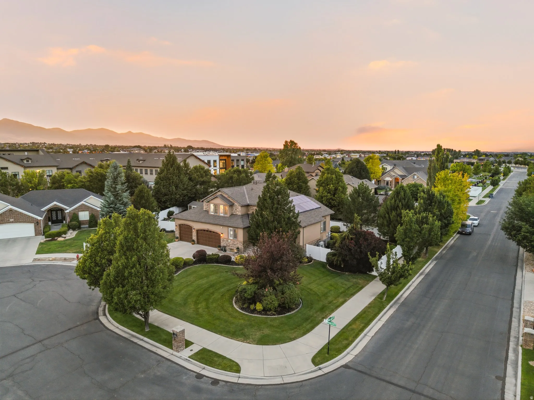 Large corner lot featuring a stucco and stone exterior, mature landscaping, a two-car garage, and solar panels