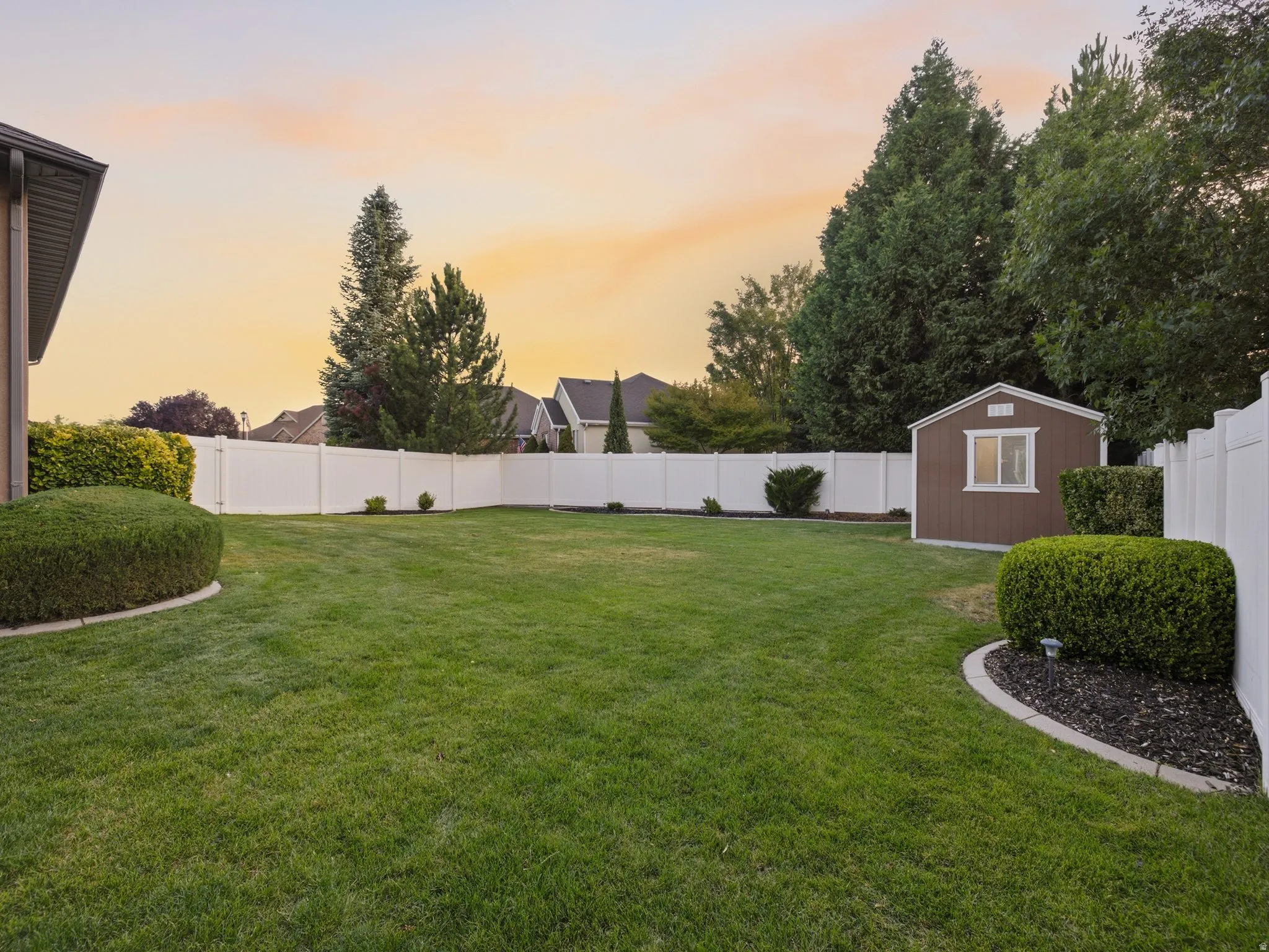 Spacious lawn area featuring a privacy fence, mature perimeter trees, and a functional storage shed
