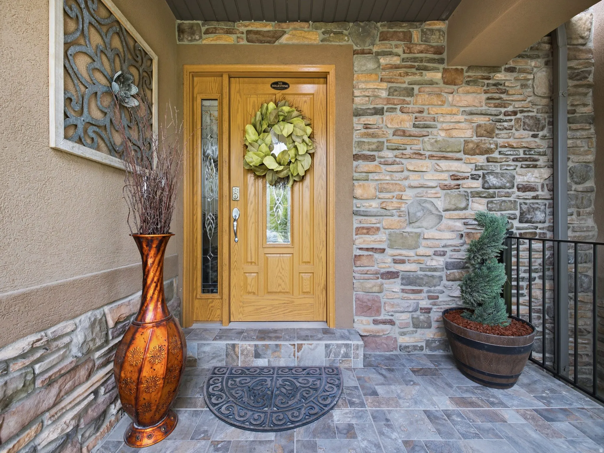 Entryway featuring a wood-panel door with sidelight, stone veneer wall accents, stucco exterior, and multi-tone tile flooring