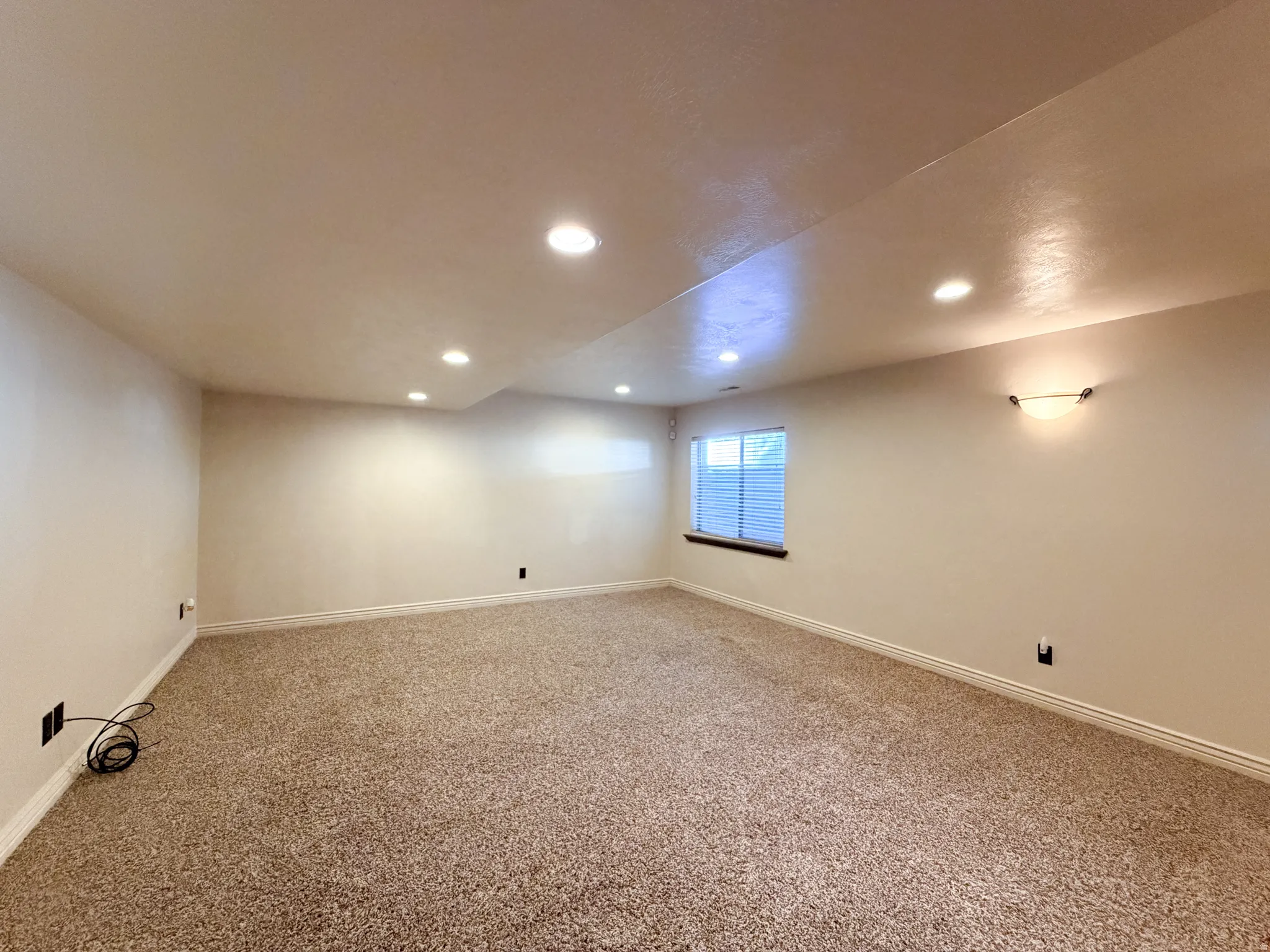 Expansive carpeted area featuring recessed lighting, a window with blinds, and a wall sconce
