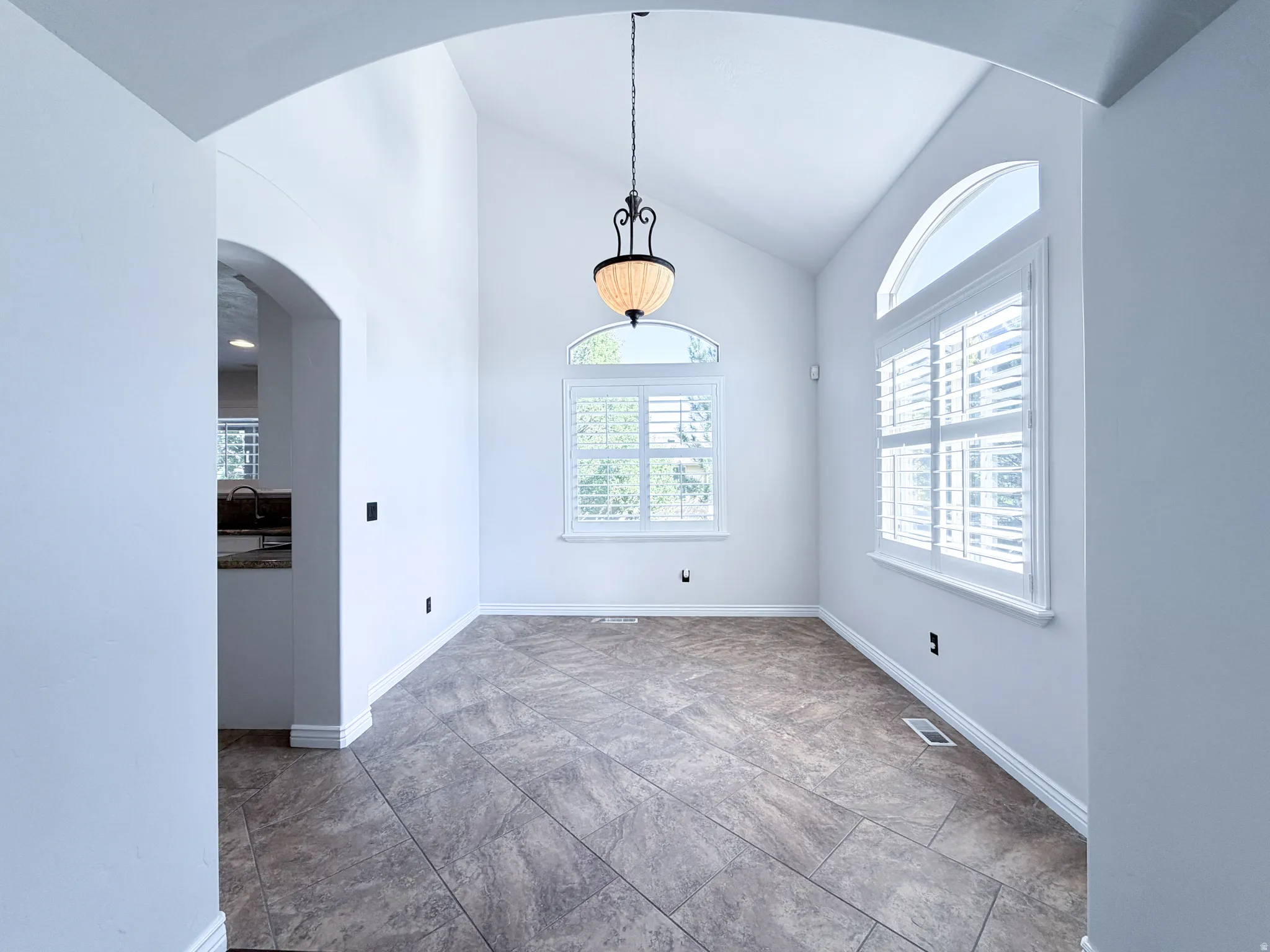 Arched entryway leading to a room with high vaulted ceilings, large windows with shutters, and a prominent hanging light fixture
