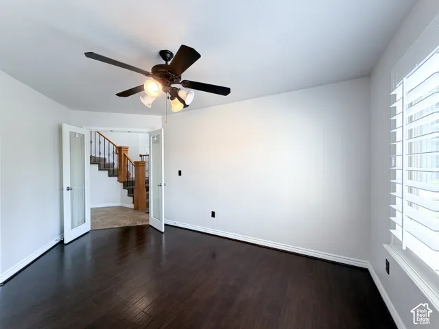 Dark wood-finish flooring with white baseboards, a ceiling fan with integrated lighting, and white plantation shutters on the window