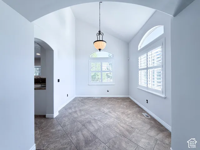Arched entryway leading to a room with high vaulted ceilings, large windows with shutters, and a prominent hanging light fixture