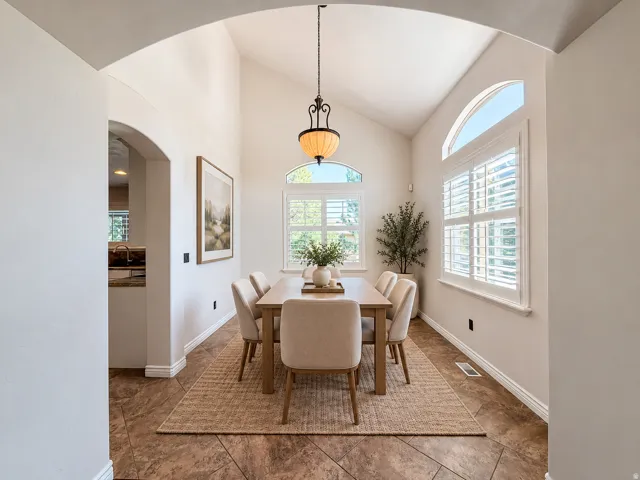 Dining area featuring vaulted ceilings, arched windows with plantation shutters, a decorative pendant light fixture, and tile flooring