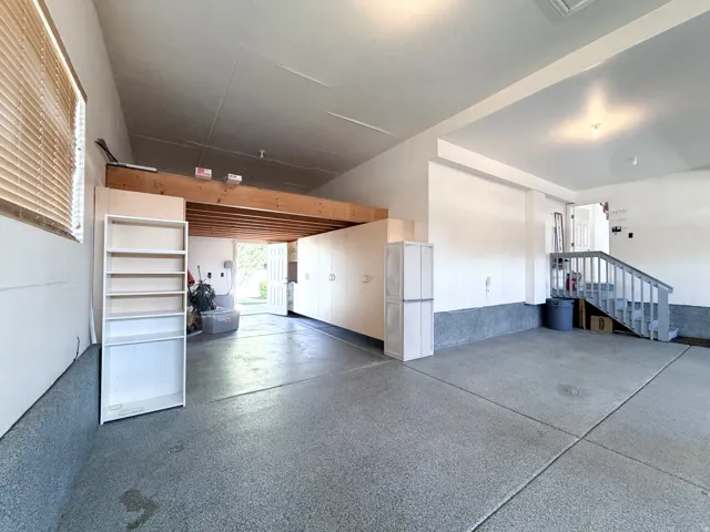 Epoxy-coated concrete flooring, built-in cabinetry, overhead storage loft, staircase access, and a large window with blinds