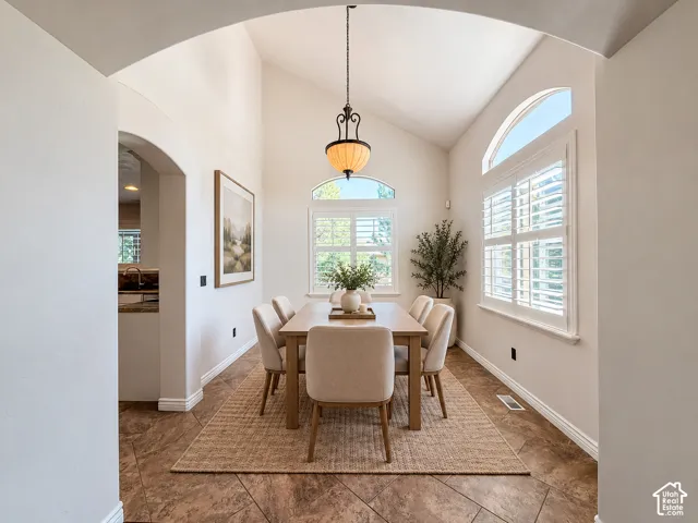 Dining area featuring vaulted ceilings, arched windows with plantation shutters, a decorative pendant light fixture, and tile flooring