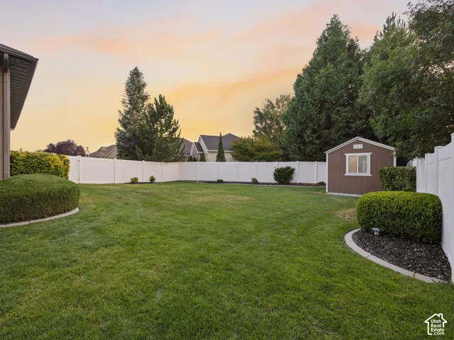 Spacious lawn area featuring a privacy fence, mature perimeter trees, and a functional storage shed