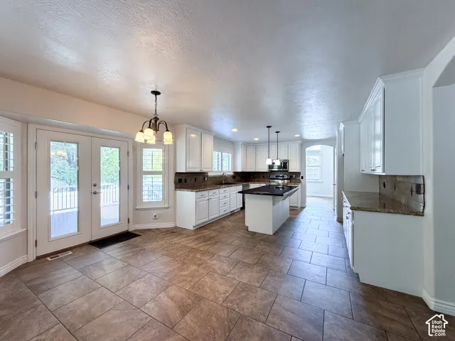 Spacious kitchen featuring white cabinetry, granite countertops, tile flooring, a central island with a dark countertop, and French doors opening to an outdoor deck