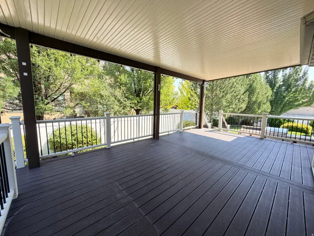 Expansive composite deck featuring dark wood-finish decking with linear board pattern, topped by a modern metal-framed pergola with integrated shade panels