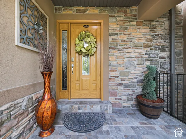 Entryway featuring a wood-panel door with sidelight, stone veneer wall accents, stucco exterior, and multi-tone tile flooring